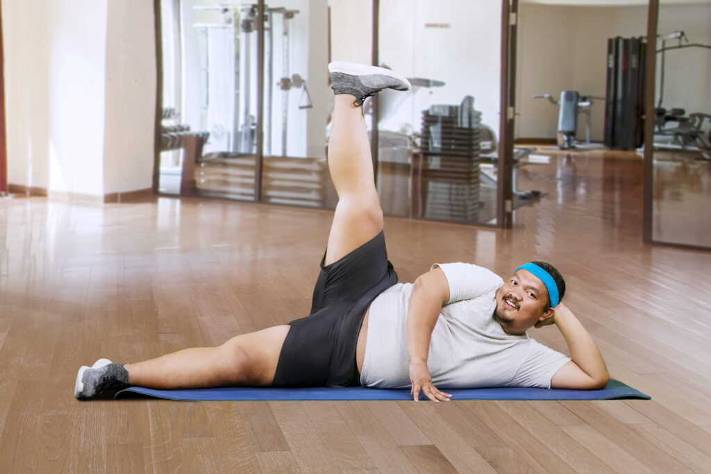 overweight asian guy doing some legs exercises sport center